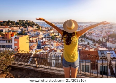 A happy tourist woman overlooks the colorful old town Alfama of Lisbon city, Portugal, and castle Sao Jorge during golden sunset time Royalty-Free Stock Photo #2172035107