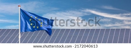 Official flag of the European Union in front of a large array of solar panels Royalty-Free Stock Photo #2172040613
