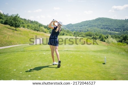Woman golf player teeing off-ball, view from behind. Sport playground for golf concept - wide landscape as background for your lettering about golf playing. Royal sport. Professional golf course 
