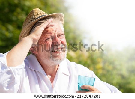 An elderly man sits outside in the great heat. He sweats and drinks mineral water. Royalty-Free Stock Photo #2172047281