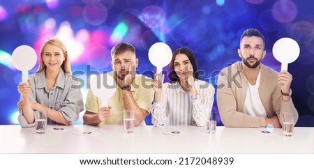 Panel of judges with different emotions holding blank signs at table against blurred background. Bokeh effect