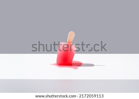 Strawberry ice lolly. Red ice cream stick melting on gray background. Summer concept