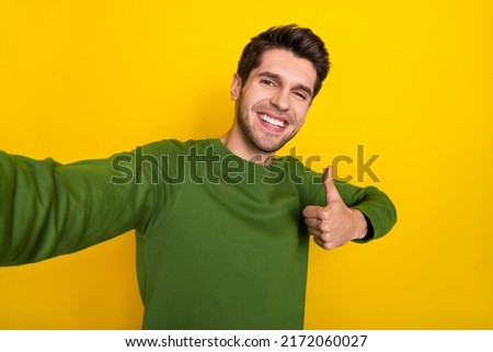 Photo of positive sweet guy dressed green pullover tacking selfie showing thumb up isolated yellow color background