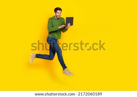 Photo of sweet attractive guy dressed green pullover jumping chatting modern gadget empty space isolated yellow color background