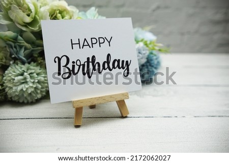 Happy Birthday text on wooden easel standing on white brick wall and wooden background