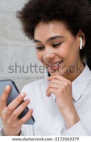 close up of happy african american woman listening music in wireless earphone and using smartphone