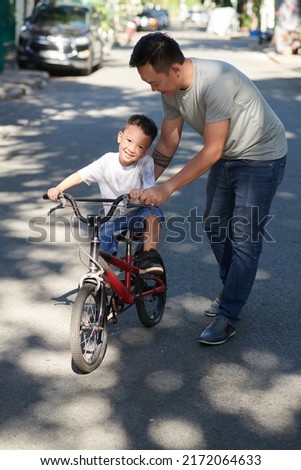 Happy father teaching smiling little son how to ride bicycle on sunny summer day