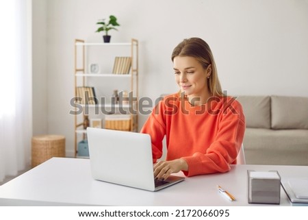 Ambitious young woman working remotely or distance learning at home using laptop. Smiling caucasian girl typing on laptop while sitting at desk in home office. Freelance or studying concept. Royalty-Free Stock Photo #2172066095