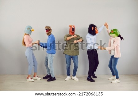 Funny diverse people in rubber animal head masks feel overjoyed dancing together on grey background. Eccentric men in women in cool headwear have fun laugh and joke. Entertainment concept.