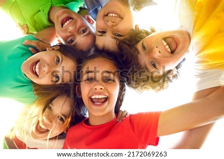Bunch of cheerful joyful cute little children playing together and having fun. Group portrait of happy kids huddling, looking down at camera and smiling. Low angle, view from below. Friendship concept Royalty-Free Stock Photo #2172069263