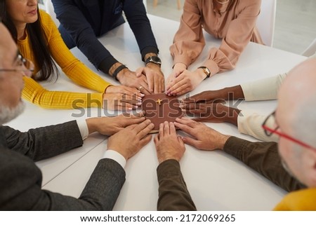 Diverse group of several different young and senior mixed race multiracial people who believe in God holding hands on the Holy Bible and praying during a religious meeting at a small Christian church