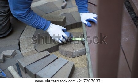 Man measuring and marking bricks for a decorative two tone paver pattern in front a stairway. Royalty-Free Stock Photo #2172070371