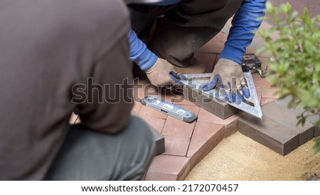 Closeup of man measuring a red brick paver for cutting to fit an edge along a rock boundary Royalty-Free Stock Photo #2172070457
