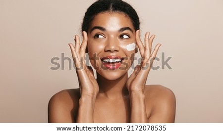 Happy smiling woman applies facial moisturizing cream, nourish her skin, stands over brown background Royalty-Free Stock Photo #2172078535