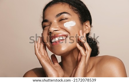 Smiling woman using skincare product. Female taking face cream to apply on facial skin Royalty-Free Stock Photo #2172078539