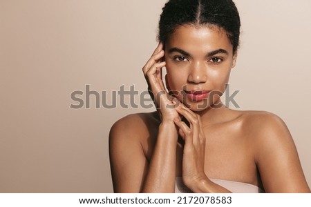 Skin care routine. Dark skinned woman with perfect glowing body, head and shoulders, touches her nourished face after skin cream and moisturizer, brown background Royalty-Free Stock Photo #2172078583