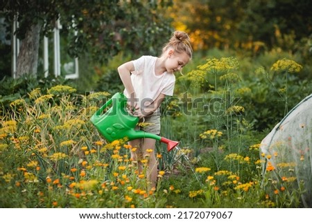 Happy child pre-teen girl with a watering can caring for flowers and vegetables in the green garden. Kids helping in the orchard Royalty-Free Stock Photo #2172079067