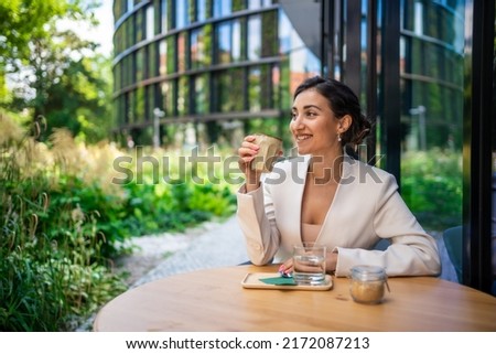 Young business woman holding and drinking coffee in street cafe in city. Portrait of beautiful woman worker waiting client on street of Prague. High quality photo