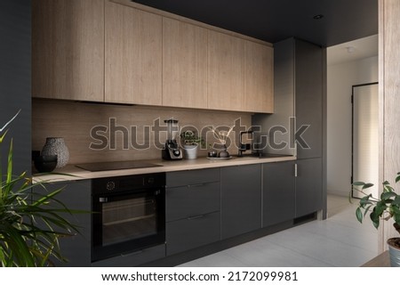 Modern and small kitchen with wooden cupboard and countertop and black furniture, oven, sink and fridge Royalty-Free Stock Photo #2172099981