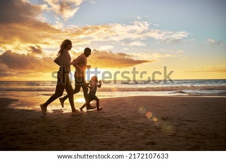 Silhouette of a carefree family running and having fun together during sunset on the beach. Parents spend time with their daughters on holiday. Little girl playing with her parents while on vacation