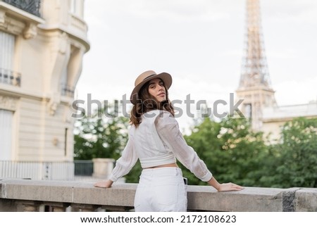 Smiling woman in sun hat looking at camera with Eiffel tower at background in Paris