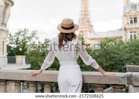 Back view of tourist in sun hat standing with blurred Eiffel tower at background in Paris