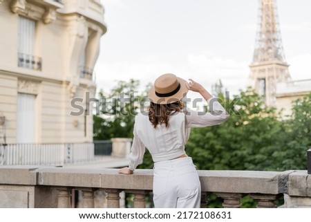 Back view of stylish woman holding sun hat with Eiffel tower at background in Paris