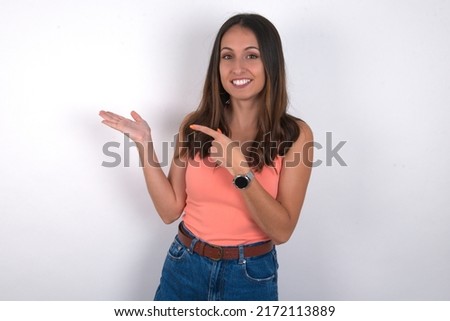 young beautiful caucasian woman wearing orange top over white background pointing and holding hand showing adverts