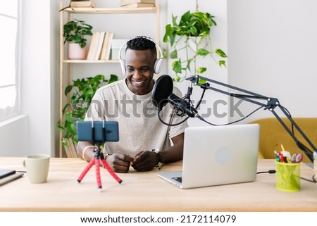 Young adult african man streaming live video at home studio - Millennial content creator male recording radio podcast - Entertainment and broadcasting concept