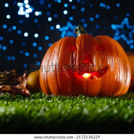 Against the background of the night starry sky, an orange pumpkin with a carved face, illuminated by a candle from the inside on green grass. Fantasy composition. Halloween.