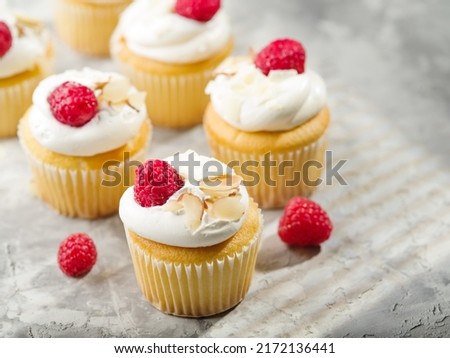 Lots of whipped cream muffins garnished with raspberries and almonds on a white background. Light sweet dessert. Restaurant, hotel, cafe, confectionery, supermarket.