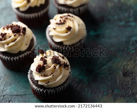 Top view of chocolate muffins topped with cream and sprinkled with grated dark chocolate on a green marble background. Holiday, birthday, delicious dessert. Banner, advertisement, invitation.