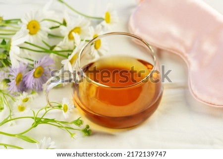 Morning, herbal tea. Concept of relaxing, self-care and good sleeping. Glass cup of tea, sleeping mask and wild flowers on a white bed linen. Summer, good morning. Soft focus style image