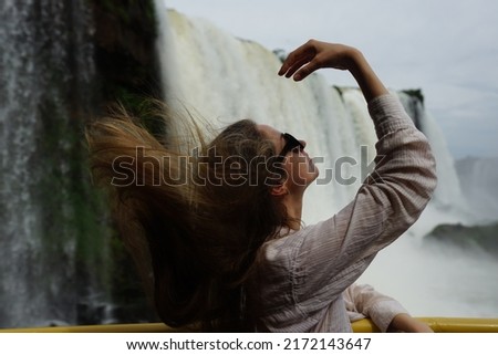 In the photo, a girl in a white shirt poses against the backdrop of Iguazu Falls — a complex of 275 waterfalls on the Iguazu River, located on the border of Brazil (Paraná state) and Argentina 
