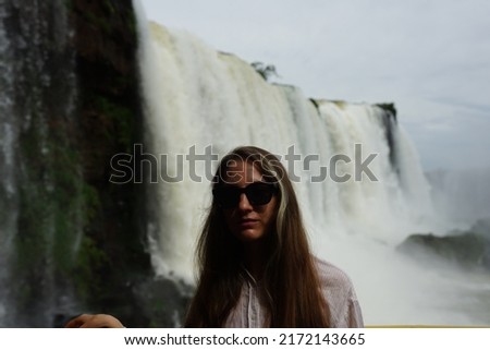 In the photo, a girl in a white shirt poses against the backdrop of Iguazu Falls — a complex of 275 waterfalls on the Iguazu River, located on the border of Brazil (Paraná state) and Argentina 