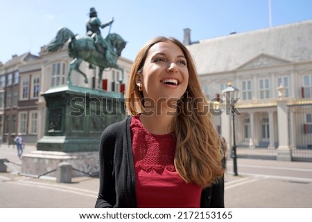 Portrait of cheerful young woman looking up to the side with Noordeinde Palace on the background in The Hague, Netherlands