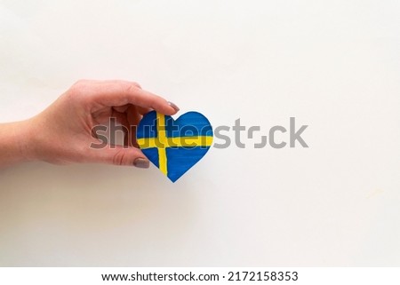 Paper heart in the colors of the flag of Sweden in female hands.