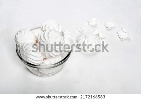 a glass vase with meringue stands on a gray background, next to a whole and broken dessert of French meringue, a horizontal picture.