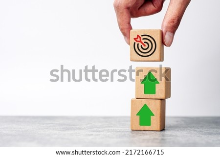 Businessman holding wooden cube with target board icon and arrow on wooden table. Goals and planning for success in marketing business, achieve the objective concept. copy space               