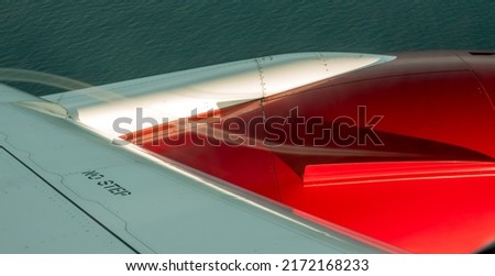 A thin stream of white water vapour follows the aerodynamic contour of a red jet engine and flows over the wing leaving a smoke trail. The fuselage says 'No Step' and the ocean can be seen below.  Royalty-Free Stock Photo #2172168233