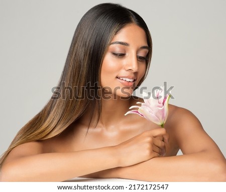 Beauty Brunette Model with Long Silk Shiny Hairstyle. Beautiful Woman looking at Flower relaxing in Spa Massage Salon. Women Face and Body Skin Care. Hair Cosmetology over White background