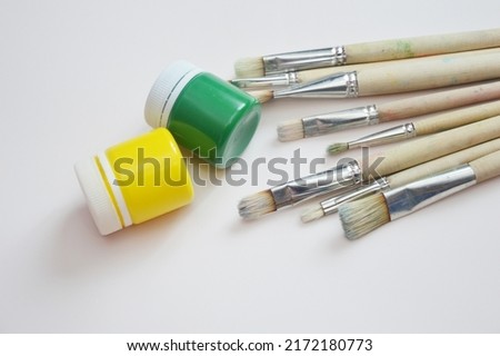 Jars of yellow and green paint and bristle brushes. Top view. Workplace for creativity. Hobbies, drawing, learning.