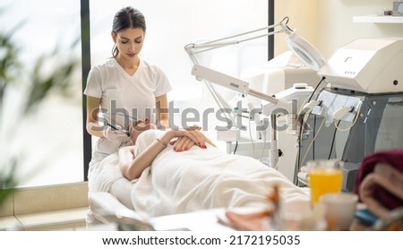 Beautician doing cosmetology procedures using radio frequency beauty machine for skin care in modern beauty salon. Royalty-Free Stock Photo #2172195035