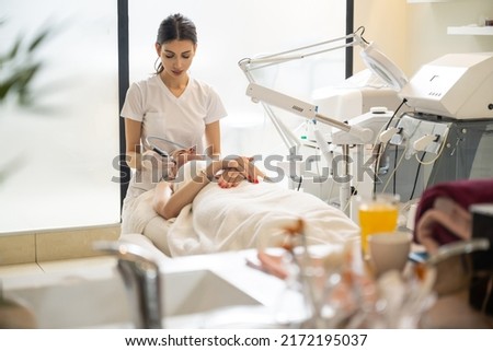Beautician doing cosmetology procedures using radio frequency beauty machine for skin care in modern beauty salon. Royalty-Free Stock Photo #2172195037