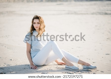 Girl. Pretty attractive slim smiling woman on a sunny beach. Girl wearing style fashion trend outfit. The Female sits on the sand on the sandy beach. The concept of summer vacation outdoors.