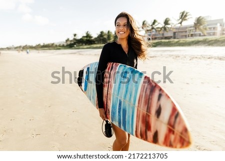 Portrait of young surfer woman on the beach holding her surfboard Royalty-Free Stock Photo #2172213705