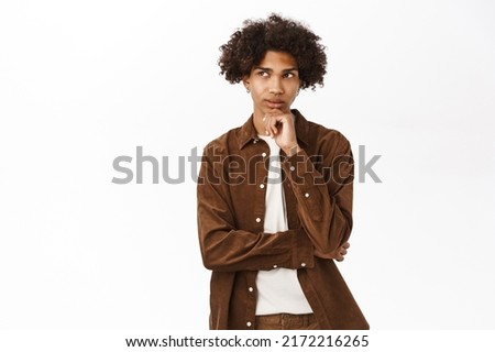 Portrait of thoughtful young man, thinking, making decision in his head, standing over white background