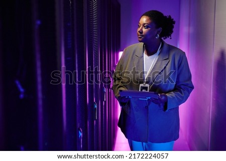 Portrait of female system administrator inspecting data network in server room lit by neon light, copy space Royalty-Free Stock Photo #2172224057