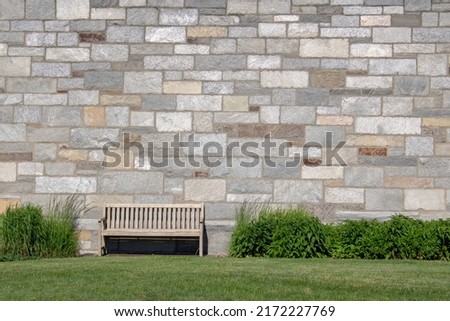 outdoor bench with rock brick wall shrubs and green grass lawn