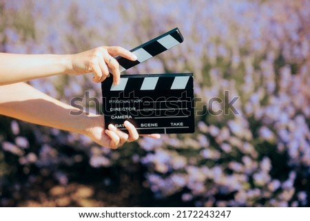
Hand Holding a Film Slate in front of a Lavender Field. Film maker producing a commercial in floral meadow during summer season
